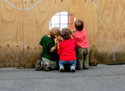 Kinder schauen durch ein Loch im Bauzaun