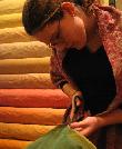 junge Dame beim Zuschneiden grüner Seide - im Hintergrund gestapelte Seide in Tönen von gelb bis rot 