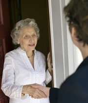 Ältere Frau gibt einer Besucherin an der Haustür die Hand