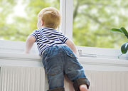 Kleinkind stützt sich auf eine Fensterbank mit Heizkörper und schaut hinaus.